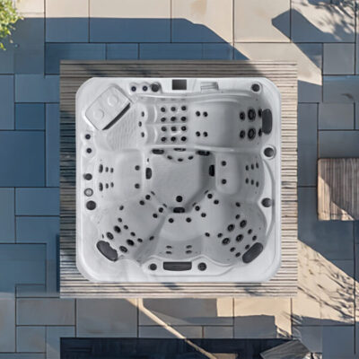 Top-down view of a square white hot tub with multiple seats and jets on a wooden deck beside a tiled patio.