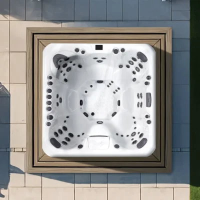 Top-down view of a white jacuzzi tub with multiple black jets set in a wooden frame on a tiled patio area.