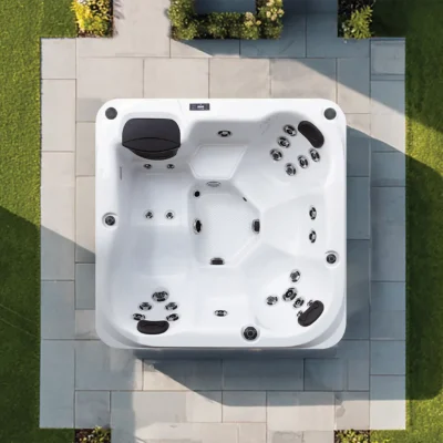 A white outdoor hot tub with multiple jets and headrests on a tiled patio, surrounded by lawn .
