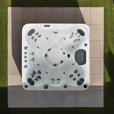 Top-down view of a white hot tub with multiple jets on a tiled patio, surrounded by green lawn and shadows.