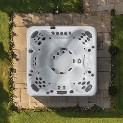 Top-down view of a large white hot tub with numerous jets, installed on a stone patio surrounded by grass and landscaping.