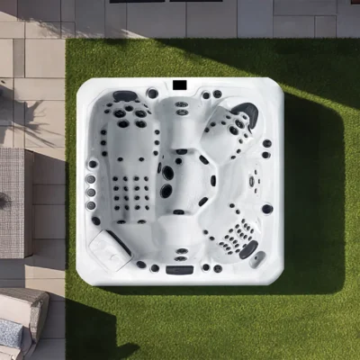 A white outdoor hot tub on a green lawn, viewed from above, with surrounding patio tiles and seating nearby.